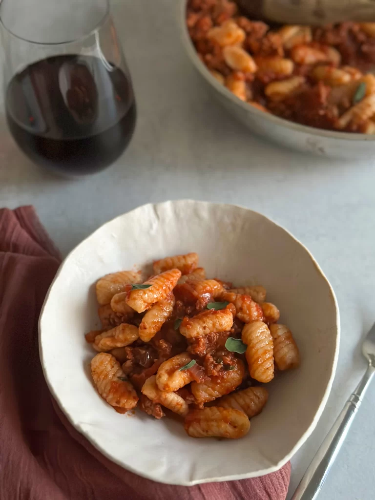 Plate of cavatelli with spicy sausage and a glass off red wine.