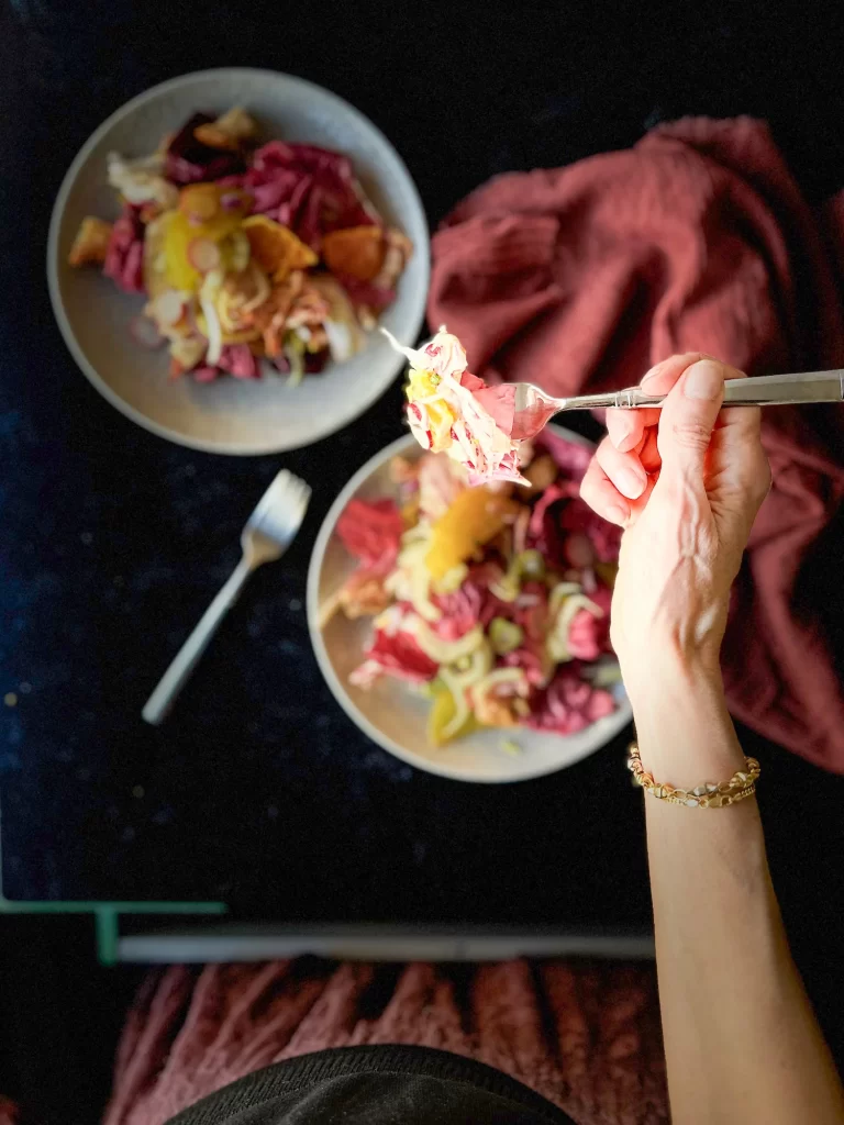 Table and woman seated while eating thee salad.